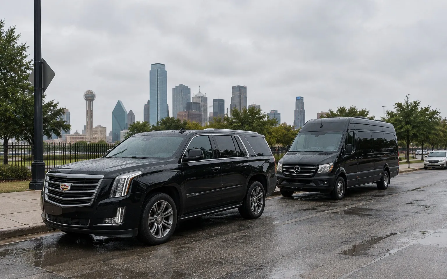 Black Cadillac Escalade and Sprinter van parked on a wet street below the Dallas skyline